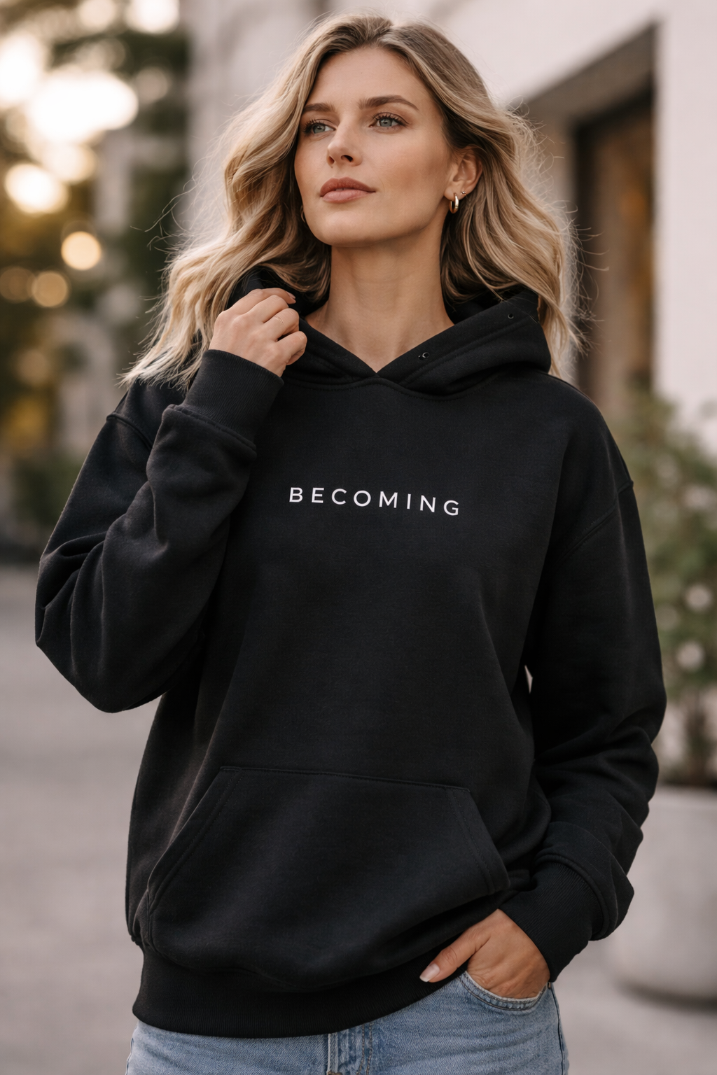 Person wearing a black hoodie with 'BECOMING' text, standing outdoors.